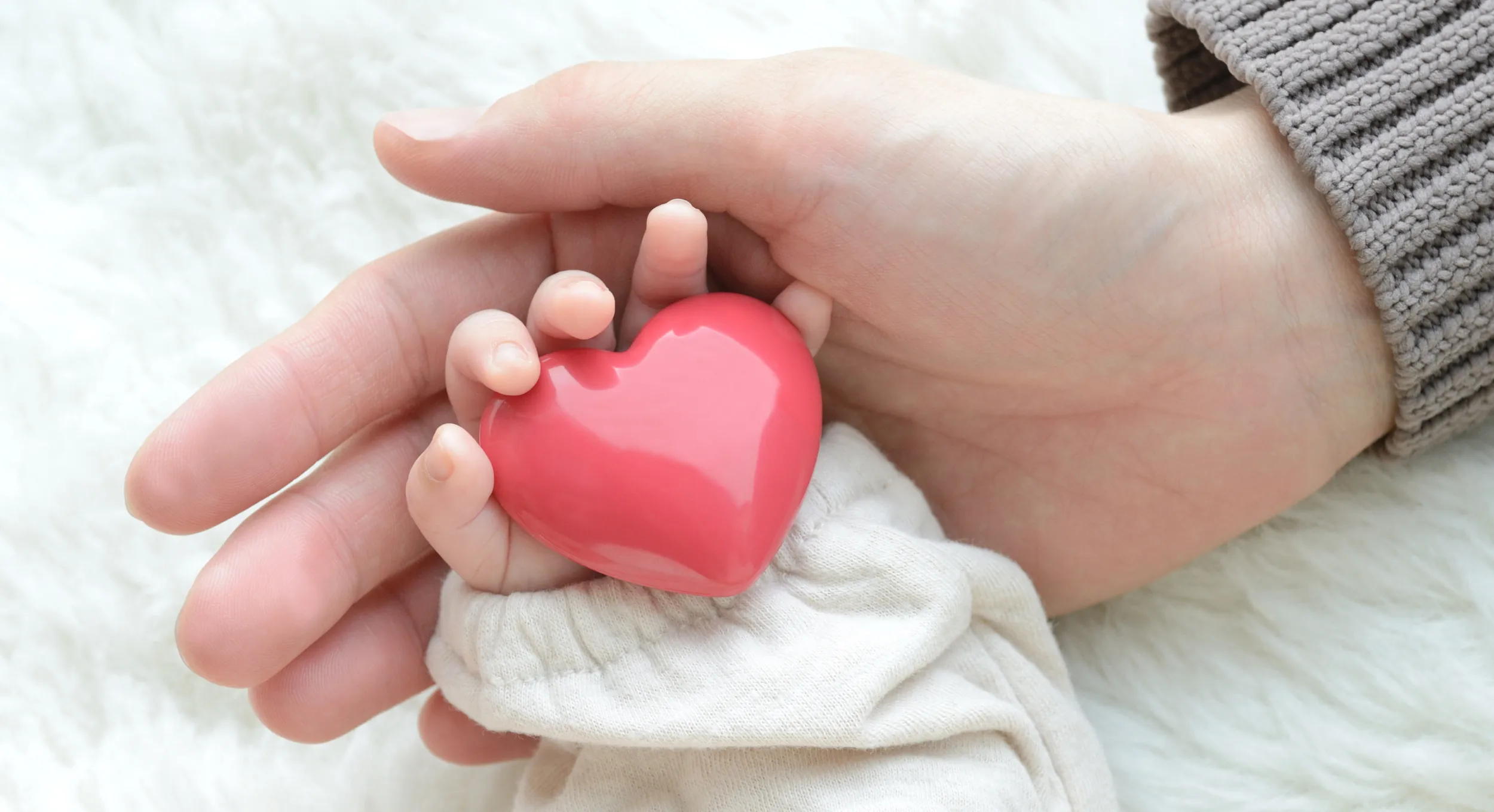 Ruce maminky a miminka svírající srdce.
